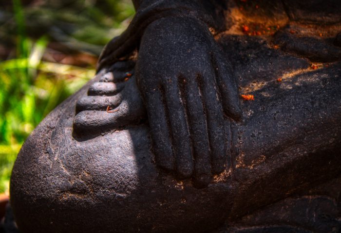 Primer plano de una mano sobre las piernas cruzadas de una estatua.
