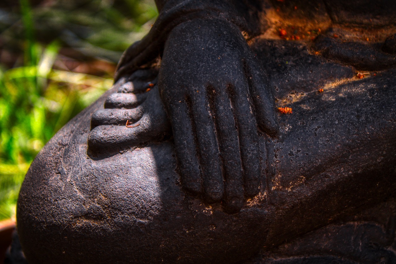 Primer plano de una mano sobre las piernas cruzadas de una estatua.