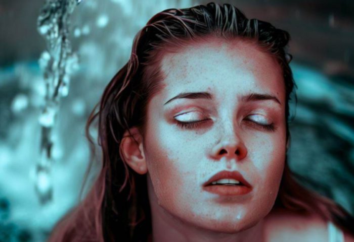 Rostro de mujer mojada con los ojos cerrados en una fuente.